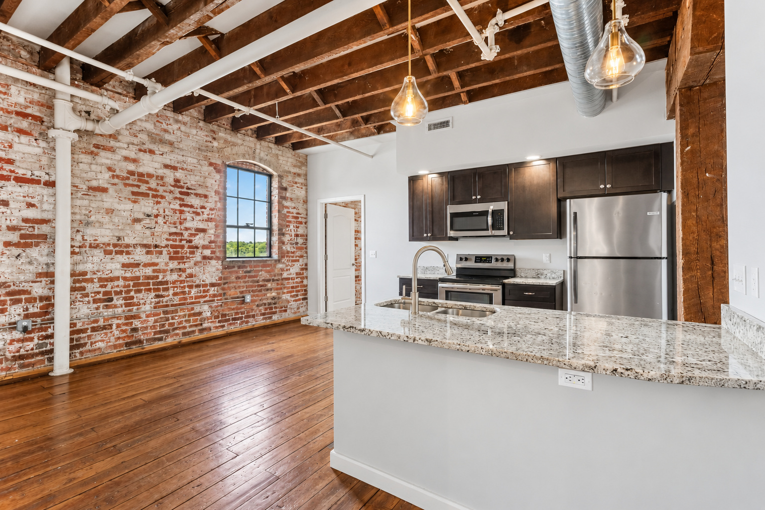 Kitchen with granite counter, pendant lights, exposed brick and arched window